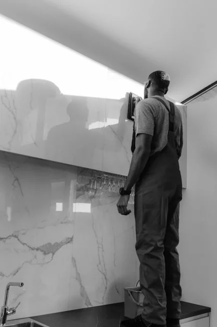 Deux femmes en tenue de travail nettoient un salon moderne à l’aide d’un aspirateur et d’une serpillière.